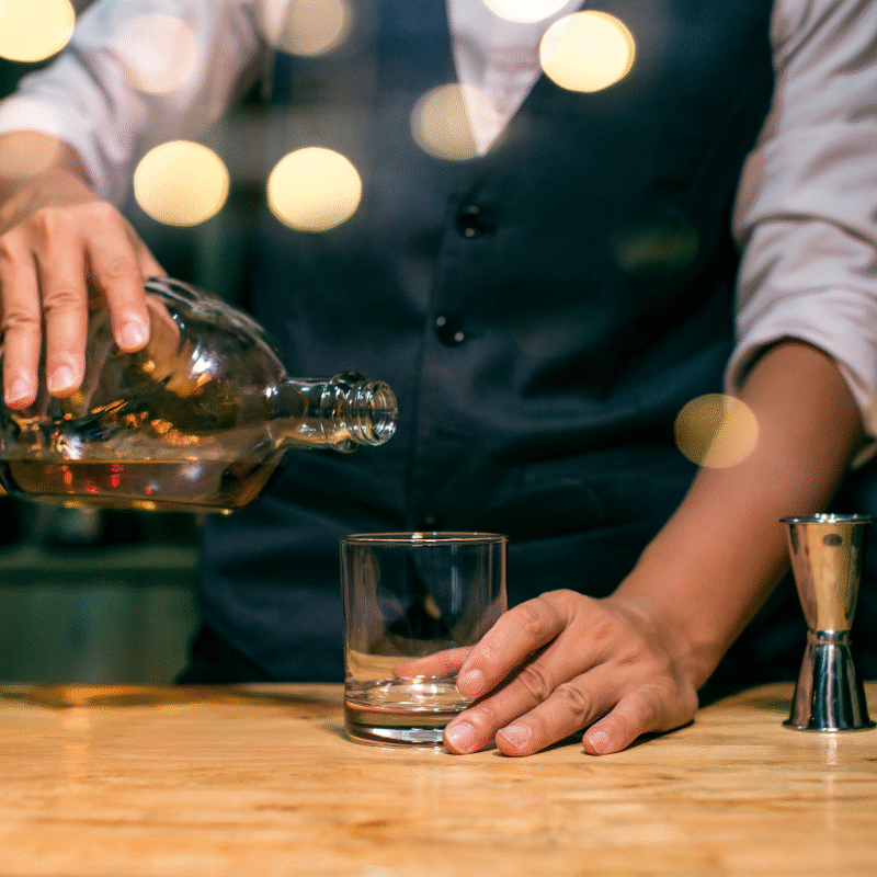 Bartender pouring whiskey into a glass during an elegant tasting session, representing the refined atmosphere of BarberNBar in Cheltenham.